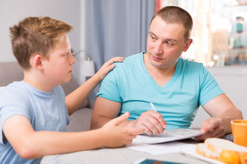 Guy with his father are working and reading documents at the home.