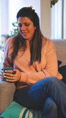 Fototapeta premium Caucasian woman holding a cup of coffee sitting on the sofa in her living room
