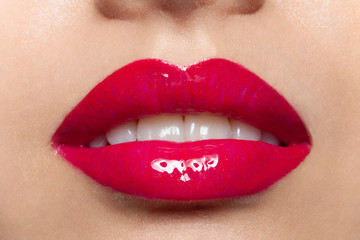 Female plump lips with red glossy lipstick closeup macro shot. Glamour fashion sensual makeup. Magenta women mouth with white teeth. Beauty, visage and cosmetics. Self-care and cosmetology
