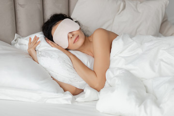 Beautiful woman sleeping seeing dreams wearing sleep mask in comfortable bed lying on soft white...