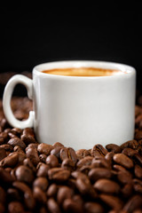 White cup of coffee with sprinkled beans. Black background. Vertical.