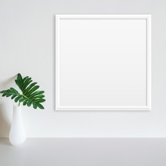 White frame mockup on white wall with philodendron leaf in vase on white surface. Copy space.