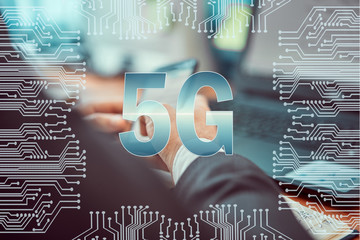 Circuit board on the background of a man working on a laptop and holding a smartphone in his hands. Caption: 5G