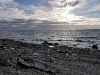 Rocky waterfront and sea with cloudy sky.