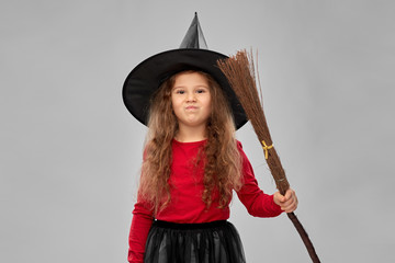 halloween, holiday and childhood concept - girl in costume and witch hat with broom over grey background