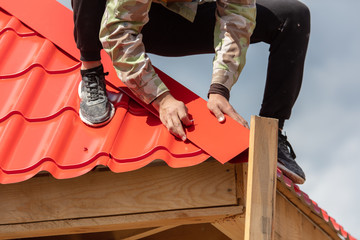 Workers install red metal tiles on the roof