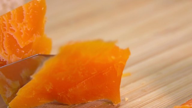 Knife cuts a hard french orange-colored Mimolette cheese on a wooden board