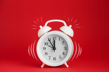 White alarm clock with imitation of the call on the red isolated background. Close-up, copy space. The concept of awakening.