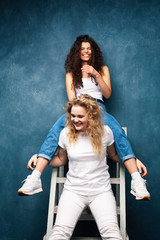 young pretty teenage girls friends with blond and brunette curly hair posing cheerful on blue background, lifestyle people concept