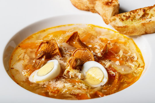 Vegeterian soup with chanterelles and vegetables with fried croutons in a white plate. Delicious recipe with wild mushrooms, organic vegetables and quail eggs. Close-up