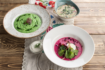 Three different traditional summer cold soups green cream soup, okroshka and red borsch on wooden table