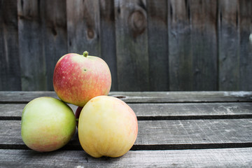 three apples in the form of a pile lie on the left on a wooden table and with free space for text on the right