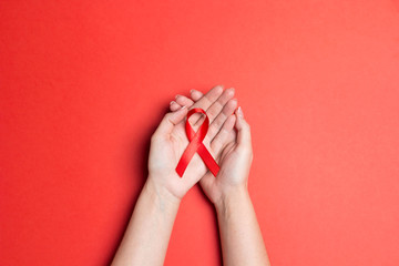 Red AIDS ribbon awareness on woman hands on red background.