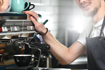 A young barista guy makes coffee on a large professional coffee machine. Small business and work concept for young people