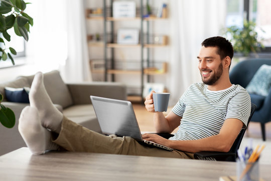 Technology, Remote Job And Lifestyle Concept - Happy Smiling Man With Laptop Computer Drinking Coffee And Resting Feet On Table At Home Office