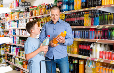 Smiling happy positive father friendly discussing with preteen boy while choosing beverages in food store
