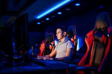 Young gamer playing video game at internet cafe or playroom, portrait, side view.