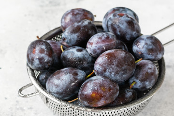 Obraz premium Ripe plum. Lots of plums in a metal bowl on a light background. Blue plums close-up. Healthy fruits