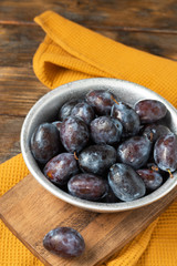 Ripe plum. Lots of plums in a metal bowl on a brown wooden table. Blue plums in a bowl close-up. Healthy fruits
