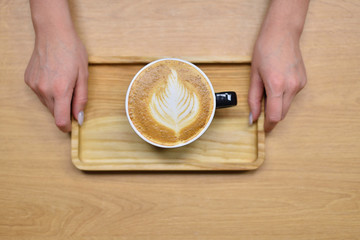 Female barista hands and a large cup of coffee with a pattern on the surface.