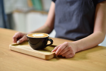 Female barista hands and a large cup of coffee with a pattern on the surface.