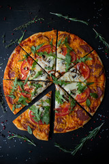 Traditional italian pizza. Cut into slices delicious fresh pizza with herbs and cheese on a dark background. Top view . Pizza on the black table.