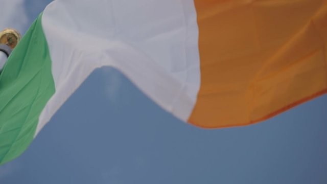Slow-motion shot of a Irish flag waving in the wind on a sunny day.