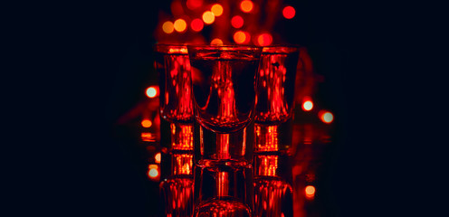 Red alcohol cocktails in shot glasses over red bokeh light and black background. Shots on bar counter in night club party.