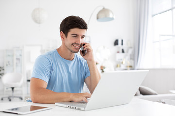 Happy man talks on phone with a laptop at office desk.