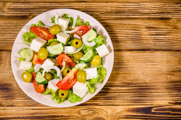 Ceramic plate with greek salad on wooden table. Top view