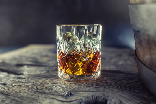 Glass with whiskey rum brandy or bourbon on an old table near a wooden barrel