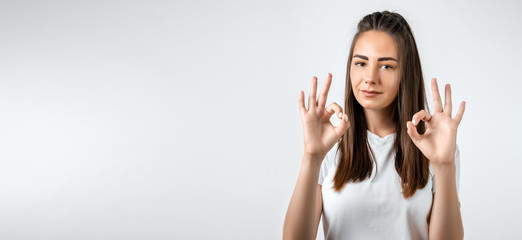 Good job! Pretty carefree modern stylish European girl with long chestnut hair making OK with both hands, gesture as if saying that everything is finee, white background. Copy space for your text