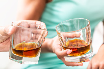 Man and woman hands toasting with glasses of whiskey brandy or rum indoors - closeup