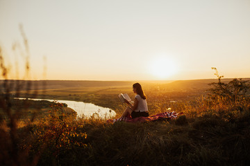 Calm girl reading a book on hill with perfect landscape, enjoying time on holiday. She read book in...