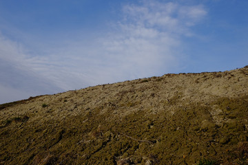 The slope of a clay hill against the backdrop of a beautiful blue sky. Lifeless soil. Sunny...