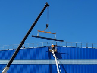 Work aerial platform and telescopic crane at work on a facade of an industrial building with a metal heavy  beam © luca piccini basile