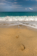 Fototapeta na wymiar wakacyjna pocztówka, gorący piasek, ślady stóp, ciepłe morze i niebieskie niebo