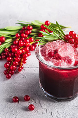 Fresh ice cold fruit cocktail in glass, refreshing summer red currant berry drink with rosemary leaf on stone concrete background, angle view