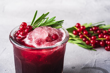 Fresh ice cold fruit cocktail in glass, refreshing summer red currant berry drink with rosemary leaf on stone concrete background, angle view macro