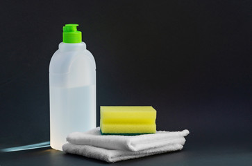 White plastic bottle for liquid household chemicals, two white rags and a sponge for washing dishes on a dark background. Concept of world cleanliness day. Close-up, copy of the space.