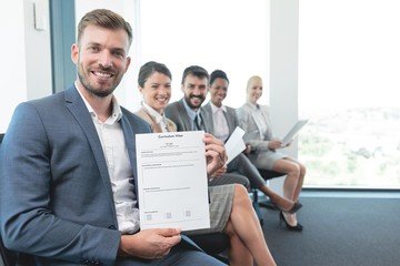 Happy businessman showing his resume while candidates are waiting in line for job interview