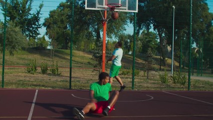 Athletic sporty mixed race street basketball player driving to the hoop with ball, committing offensive foul of charging against opposing defender while playing basketball game on outdoor urban court.
