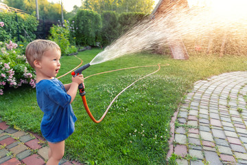 Cute adorable caucasian blond toddler boy enjoy having fun watering garden flower and lawn with...