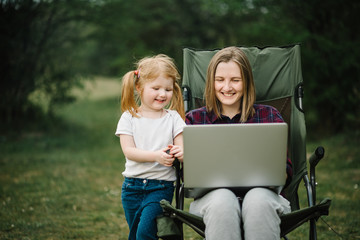 Chat online with family on laptop on picnic in nature. Homeschooling, freelance job. Mom and child. Mother work on Internet with kid outdoors. Quarantine, closed nursery school during coronavirus.