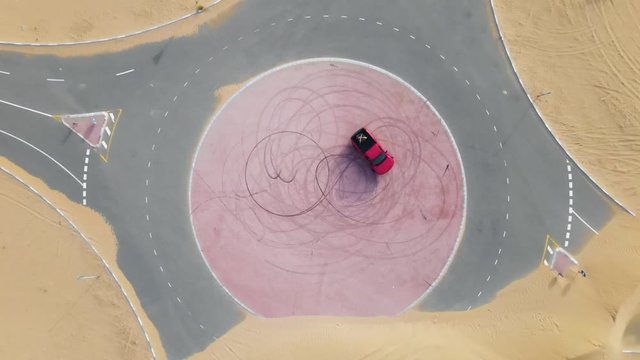 Top down drone view of a red truck drifting on a roundabout in the middle of the desert.