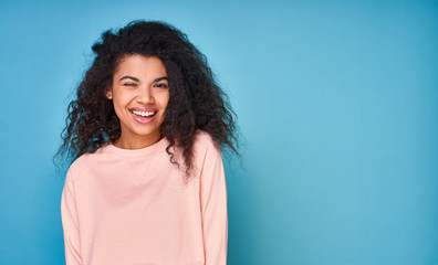 Fototapeta premium Winking cute African-American woman with curly hair on a blue background.