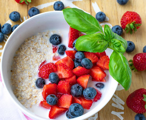Overhead view of an oatmeal with berries in a white bowl with basil leaf