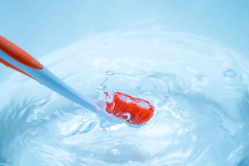 Orange toothbrush in lue pure water with splashes. Dental care concept