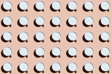A group of white ceramic mugs with milk on a beige background. Pattern with hard shadows. Coffee shop breakfast concept
