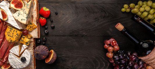selection of cheeses, figs, nuts and bottle of wine on a wooden tabe. Above view banner. copy space. Top view